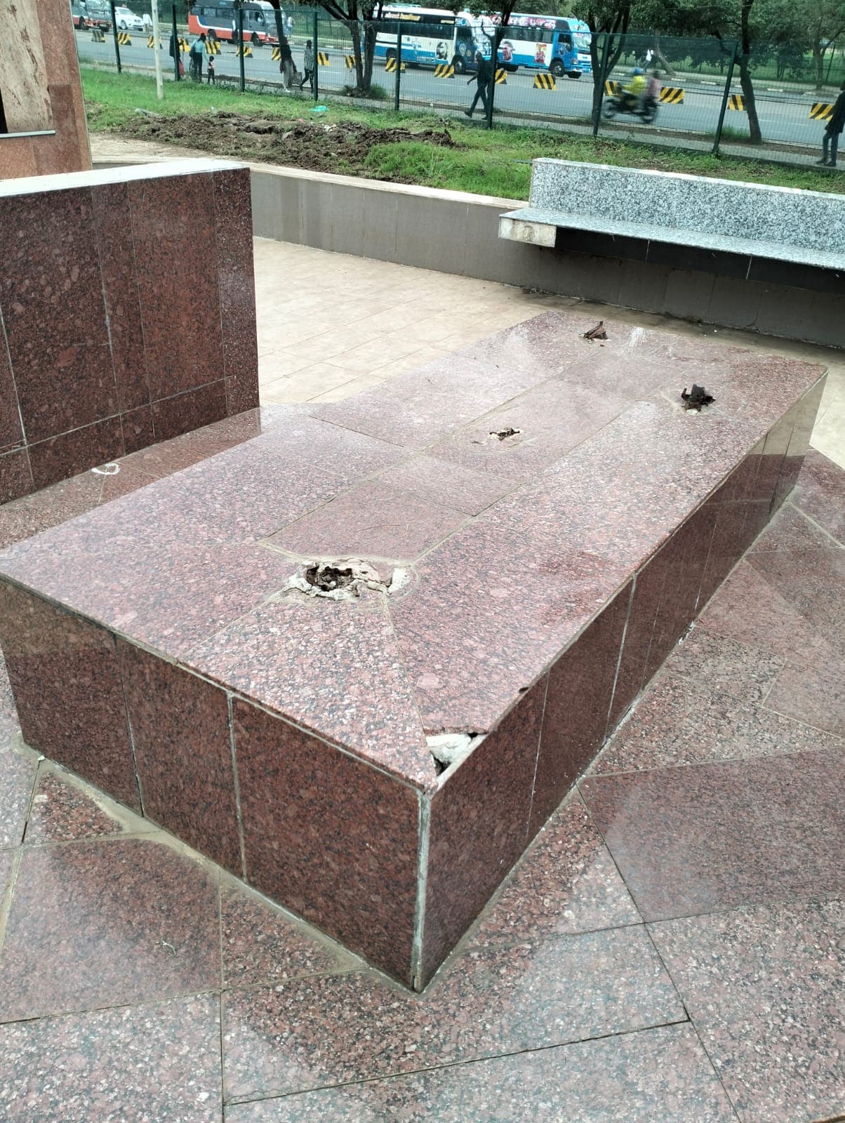 A granite-clad plinth with cracked tiles and corroded fixings, stripped back for repair